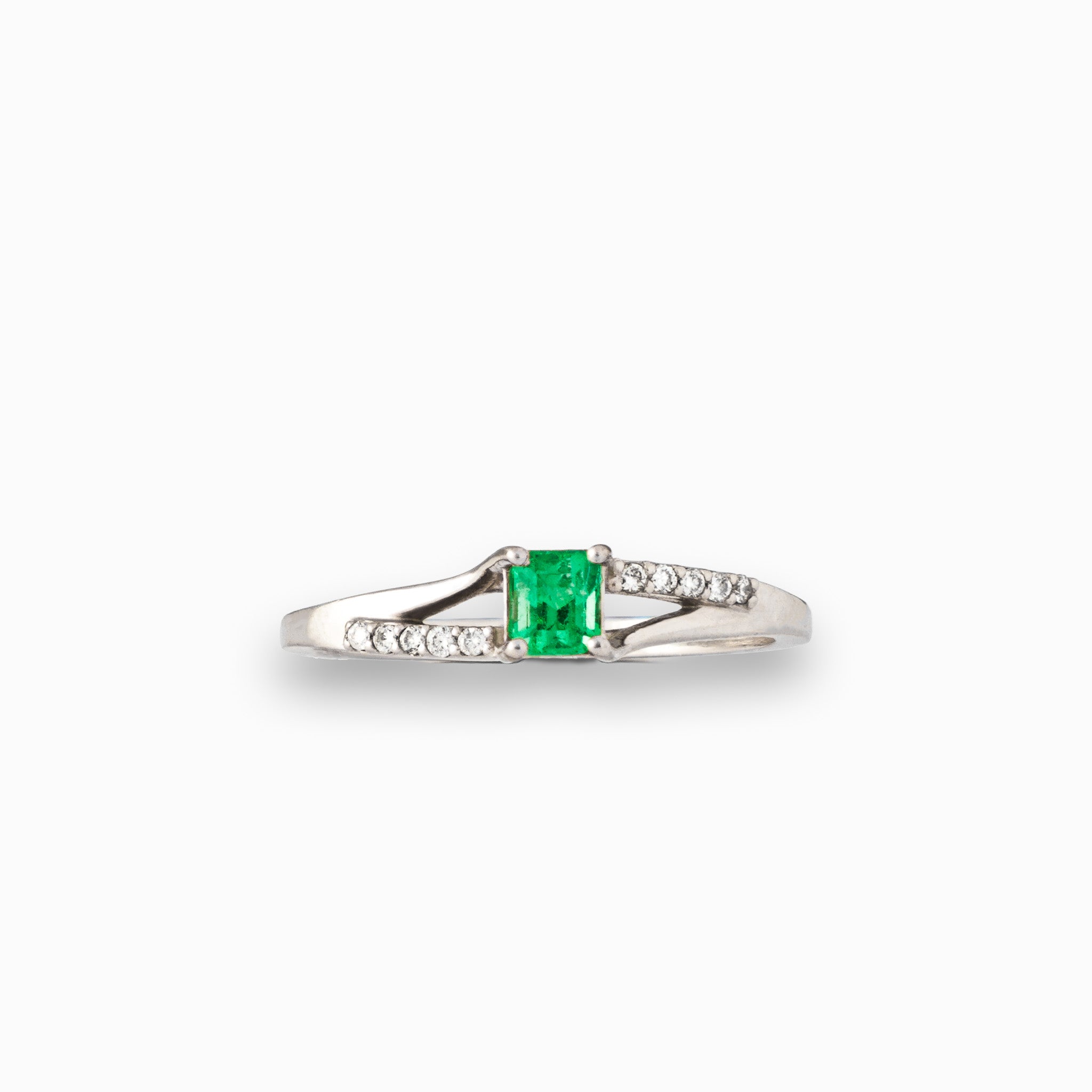 Anillo de plata paladio con esmeralda central de 0.32ct y diamantes laterales en movimiento bypass sobre fondo blanco.