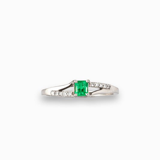 Anillo de plata paladio con esmeralda central de 0.32ct y diamantes laterales en movimiento bypass sobre fondo blanco.