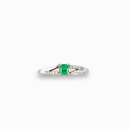  Anillo de plata paladio con esmeralda central de 0.32ct y diamantes laterales en movimiento bypass sobre fondo blanco.
