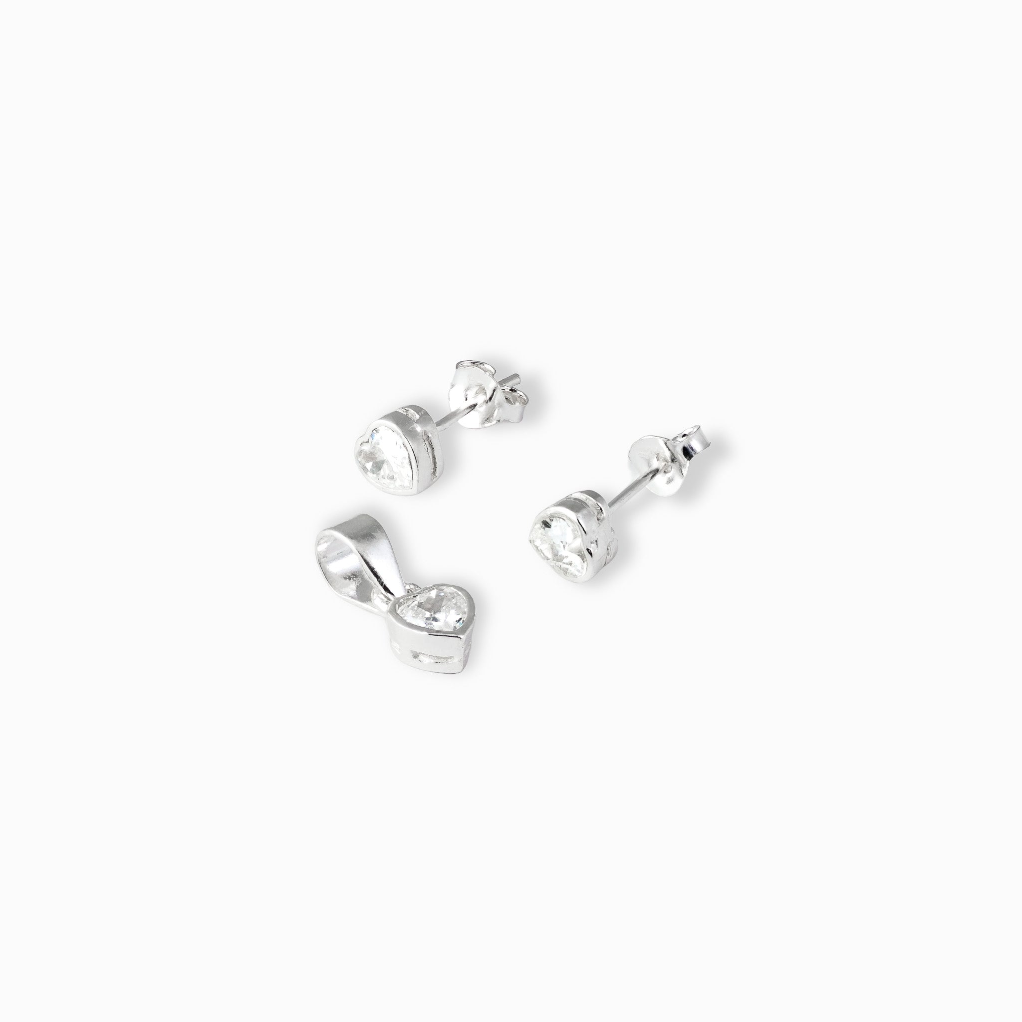 Juego de joyería en plata ley 925 que incluye aretes de topo y dije en forma de corazón con circón transparente de 5 mm sobre fondo blanco.
