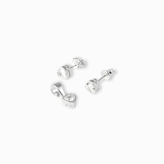 Juego de joyería en plata ley 925 que incluye aretes de topo y dije en forma de corazón con circón transparente de 5 mm sobre fondo blanco.
