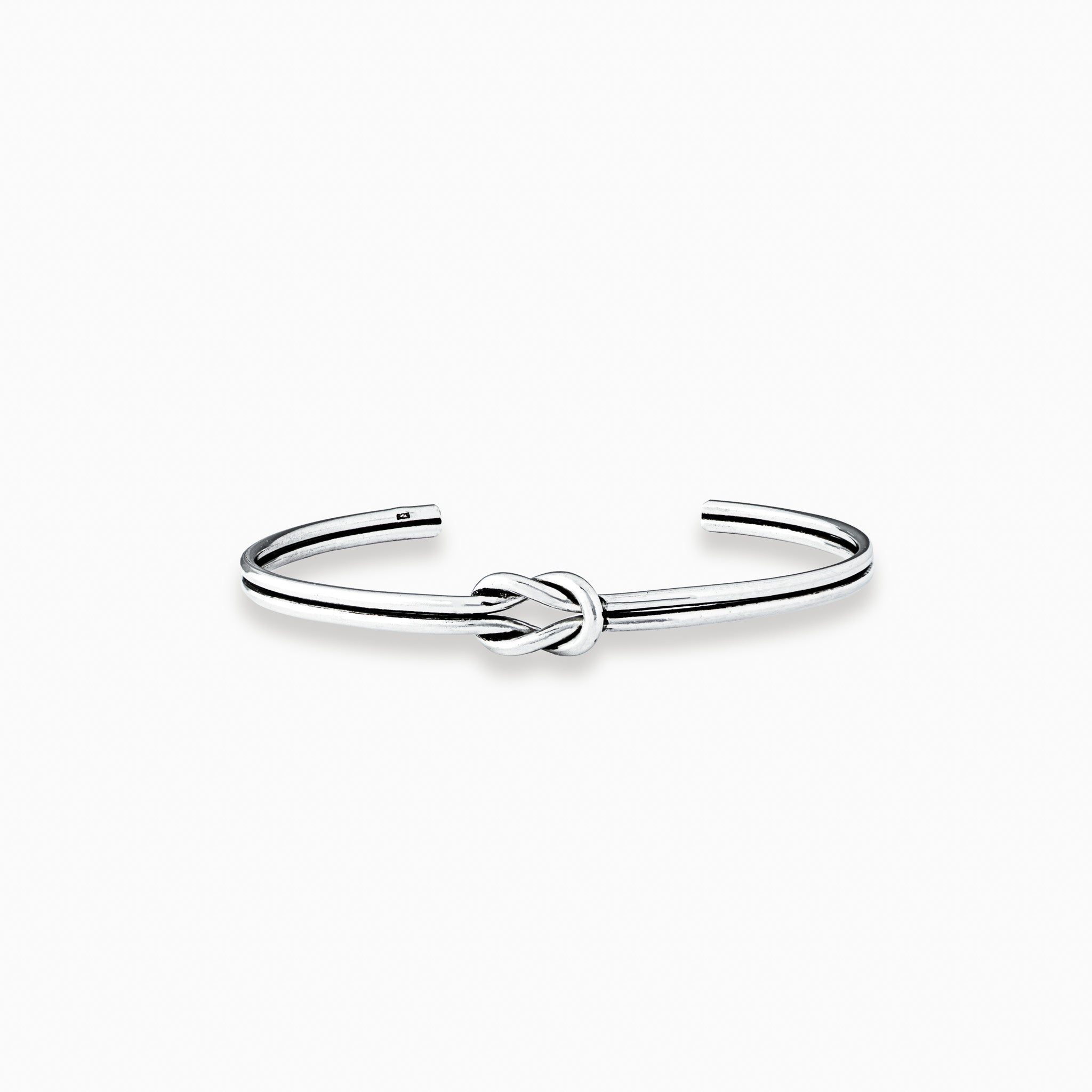 Pulsera rígida tipo aro con detalle de nudo central elaborada en plata ley 925 de 4 mm de grosor sobre fondo blanco.
