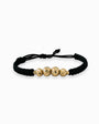 Pulsera tejida de color oscuro para adulto con cuatro balines de oro 18k de acabado diamantado (7mm y 6mm) sobre fondo blanco.

