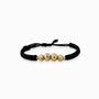 Pulsera tejida de color oscuro para adulto con cuatro balines de oro 18k de acabado diamantado (7mm y 6mm) sobre fondo blanco.
