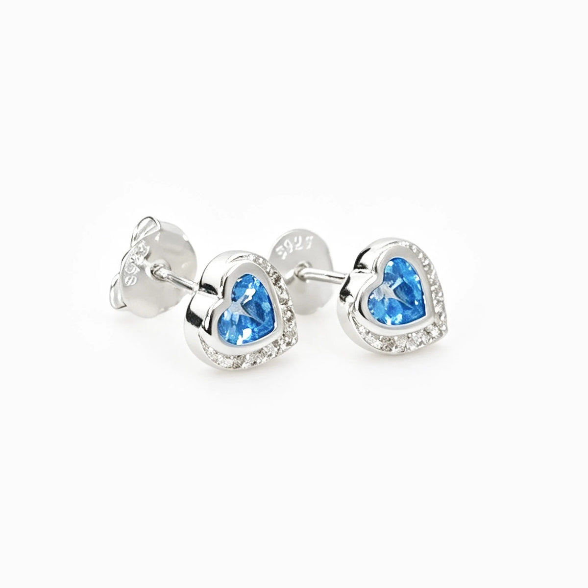 Set de topos y dije con forma de corazón en plata ley 925 con circones azul claro y halo brillante.
