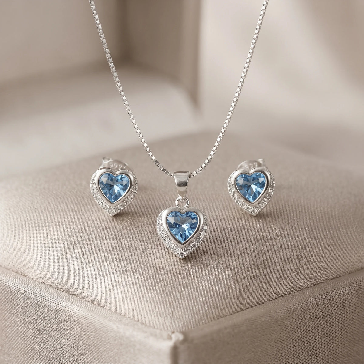 Set de topos y dije con forma de corazón en plata ley 925 con circones azul claro y halo brillante.