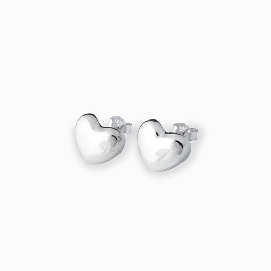 Par de aretes tipo topo con forma de corazón liso y brillante elaborados en plata ley 925 de 12 mm de ancho sobre fondo blanco.
