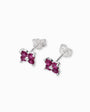 Par de aretes tipo topo con forma de flor de cuatro pétalos elaborados en plata ley 925 con circones rojos brillantes sobre fondo blanco.